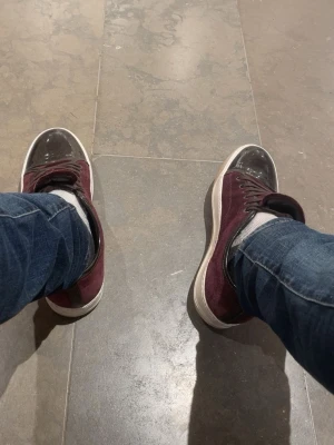 Vinröda sneakers med svarta detaljer - Snygga vinröda sneakers med svarta detaljer och vita sulor. Skorna har klassisk låg design med snörning och ovandel i mockaliknande material. Perfekta för dig som vill ha en stilren och trendig look.  