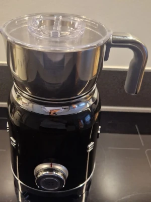 Smeg mjölkskummare svart och silver - Snygg mjölkskummare från Smeg i svart och silver. Maskinen har en rundad retrodesign, metallkanna med handtag och genomskinligt lock. Perfekt för att fixa cappuccino eller varm choklad hemma. Passar bra i köket för dig som gillar stilrena köksprylar.