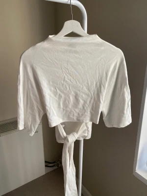 Vit croppad topp med knyt - Säljer en vit croppad topp med korta ärmar och knytband i midjan. Toppen har en enkel och clean design som passar perfekt till jeans eller kjol. Materialet känns mjukt och lätt, vilket gör den skön att bära under varmare dagar.