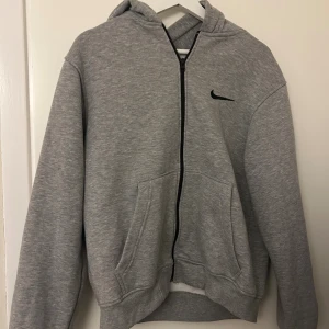 Grå zip-hoodie från Nike - Snygg grå hoodie från Nike med dragkedja framtill och svart logga på bröstet. 