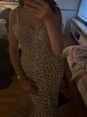 Champagnefärgad paljettklänning - Säljer en lång, champagnefärgad klänning med smala axelband och v-ringning. Klänningen är täckt av glittriga diamanter och har ett elegant, figurnära snitt som framhäver siluetten. Perfekt för dig som vill sticka ut på bal eller fest. ⚠️PRIS KAN DISKUTERAS 