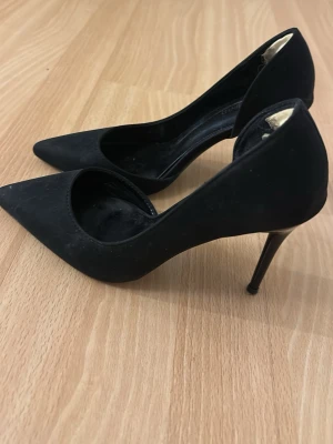 Svarta spetsiga pumps med klack - Säljer ett par klassiska svarta pumps med spetsig tå och smal klack. Skorna har en elegant siluett och är tillverkade i ett matt material. Perfekta för dig som gillar stilrena och tidlösa skor.