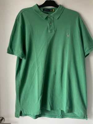 Grön pikétröja från Polo Ralph Lauren - Säljer en klassisk grön pikétröja från Polo Ralph Lauren med krage och knappar framtill. Tröjan har korta ärmar och den ikoniska broderade loggan på bröstet. Perfekt för dig som gillar stilrena och tidlösa plagg.