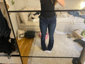 Mörkblå bootcut jeans - Säljer ett par mörkblå bootcut jeans med klassisk femficksdesign och normal midja. Jeansen har en snygg tvätt och är tillverkade i ett stretchigt denimtyg som sitter bekvämt. Från hollisyer och i bra skick.