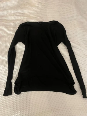 Svart långärmad tröja - En enkel och stilren svart långärmad tröja med rund halsringning. Tröjan har en något lös passform och är tillverkad i ett tunt, mjukt material som känns skönt mot huden. Perfekt att matcha med jeans eller kjol för en clean look.