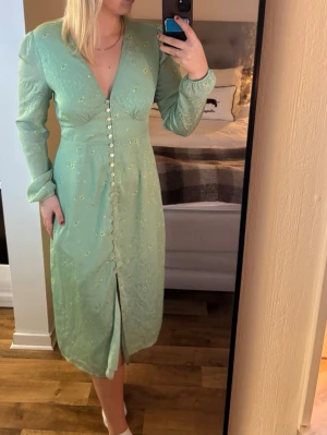 Mintgrön blommig långklänning Adoore - Mintgrön långklänning från Adoore  med små blommor, v-ringad och långa ärmar. Klänningen har knappar framtill hela vägen ner och en liten slits nedtill. Endast använd en gång och passar mer 38/ M skulle jag säga
