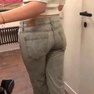 Ljusgrå raka jeans med hög midja - Säljer ett par ljusgrå jeans med raka ben och låg midja. Jeansen har klassiska fem fickor och bälteshällor. Materialet är denim och de har en enkel, stilren look utan slitningar eller dekorationer. Perfekta för en clean och avslappnad stil.