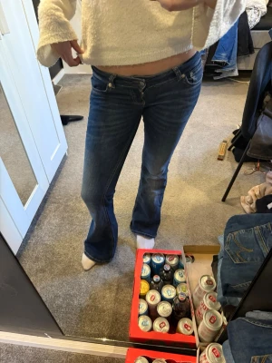 Blå bootcut jeans med låg midja - Snygga blå bootcut jeans med låg midja och klassiska fem fickor. Jeansen har en lätt tvättad look och sitter tajt över låren för att sedan släppa ut vid bensluten. Perfekta för en avslappnad och trendig stil.