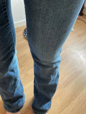 Blå bootcut jeans i denim - Säljer ett par klassiska blå bootcut jeans i mjuk denim med lätt slitningar på låren. Jeansen har normal midja och raka ben som går ut lite nedtill. Perfekta för en avslappnad och trendig look.