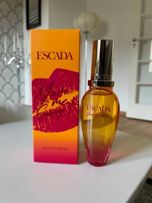 Escada Yum me sunny 30 ml - Fräsch parfym från Escada, Yum me sunny, i en snygg orange och rosa glasflaska med gulddetaljer. Doften har inslag av passionsfrukt, kokosmjölk och ylang ylang. Förpackningen är färgstark med läppmotiv och text i rött och gult. Innehåller 30 ml Eau de Parfum. Testat ett spray!