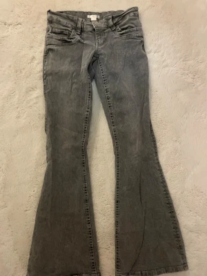 Gina tricot low waist bootcut - Snygga grå jeans med bootcut-modell och låg midja. Klassisk femficksdesign och slitna detaljer för en cool vintagekänsla. Perfekta för dig som gillar retrostil och vill ha ett par bekväma jeans i bomull.