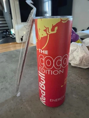 Red Bull Orange / Röd Termosmugg 0.6L - Stor termosmugg med Red Bull Coconut Edition-tryck i rött, vitt och gult. Cylindrisk form med genomskinligt lock och sugrör. Perfekt för drycker och har en cool energidrycksdesign som sticker ut. Rymmer 20oz / ca 0.6L och håller värme/kyla extremt länge! 