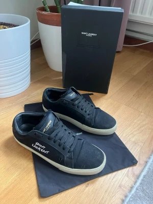 Svarta Saint Laurent sneakers - Snygga svarta sneakers från Saint Laurent med vit logga på sidan och tungan. Följer med box och dustbag. Vid mer frågor är det bara att skriva! Inte äkta🌟därav priset☺️