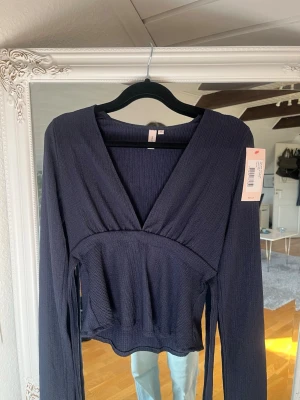 Mörkblå omlottopp med knyt - Trendig mörkblå omlottopp med v-ringning och långa ärmar. Toppen har ribbad struktur och ett snyggt knyt i midjan som markerar siluetten. Perfekt att styla med både jeans och kjol för en cool look.