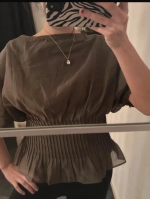 Zara Khaki blus - Snygg olivgrön topp med korta ärmar och smockad midja som ger en markerad siluett. Helt ny med prislapp kvar, nypris 599kr. Säljer för att jag köpte fel storlek.