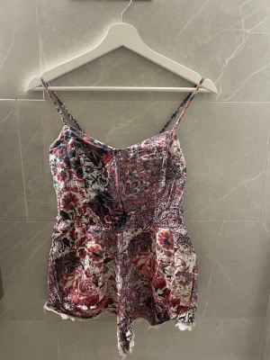 Mönstrad jumpsuit med spetsdetaljer - Säljer en snygg body med tunna axelband och v-ringning som ger en liten push upp med eller utan bh. 