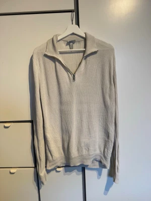 Beige stickad halvzip från H&M - Säljer en beige stickad tröja från H&M med halvzip och hög krage. Tröjan har ribbstickad struktur, långa ärmar och avslappnad passform. Perfekt för lager på lager och enkel att matcha med olika outfits. Den är i storlek S men passar även M.