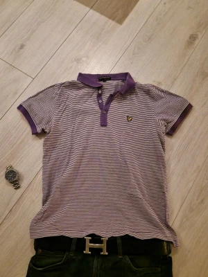 Vintage randig pikétröja Lyle & Scott - Säljer en klassisk pikétröja från Lyle & Scott i lila och vitt med smala ränder. Tröjan har korta ärmar, krage och knappar framtill samt den ikoniska loggan på bröstet. Perfekt till jeans eller shorts för en avslappnad look. Denna pikétröja är väldigt retro och fet. Fint skick, kicka in mina andra annonser. Ha det🤟  