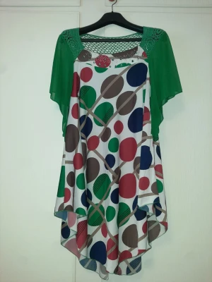 Färgglad kortklänning med gröna ärmar - Unik kortklänning med gröna kortärmar och färgglatt prickigt mönster i rött, grönt, blått och brunt. Klänningen har meshdetaljer upptill och lös passform. Perfekt för dig som gillar färg och lekfull stil.