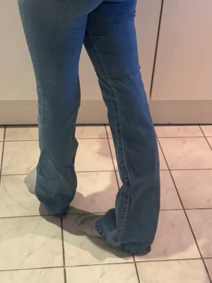 Blå bootcut jeans med hög midja - Säljer ett par blå bootcut jeans med hög midja och klassisk femficksdesign. Jeansen har en snygg tvätt och lätt utsvängda ben som ger en retrovibe. Perfekta att styla med sneakers eller boots för en cool look. Hög fickor så man får en jättefin rumpa. Stretchiga gör de väldigt bekväma att ha på sig.