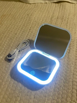 Fickspegel  - Fin liten fickspegel med lampa. Tre olika ljusstyrkor och två speglar, en normal och en inzoomad. Sladd medföljer.  Mått när den är stängd: Höjd: 8cm, längd: 9cm