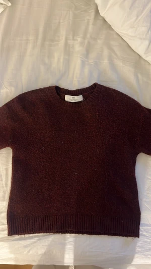 Vinröd stickad tröja från H&M - Mysig vinröd stickad tröja från H&M med rund halsringning och ribbade muddar. Tröjan har en croppad passform och är perfekt för lager på lager. Materialet är mjukt och värmande, vilket gör den idealisk för kyligare dagar. Storlek 122/128 men sitter som en vanlig xs
