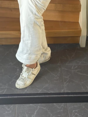 Vita sneakers från Valentino  - Snygga vita sneakers från Valentino med guldfärgade nitar. Skorna har klassisk låg modell, rund tå och vita snören. Perfekta för dig som gillar en stilren men ändå trendig look.