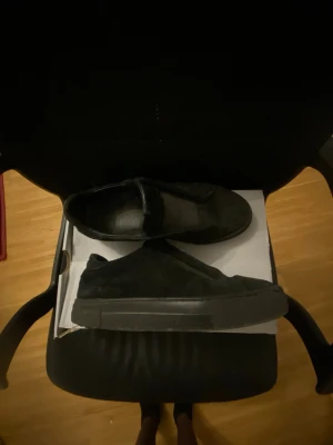Axel arigato skor  - Säljer ett par helsvarta slip-on sneakers med ovandel i mocka och gummisula. Skorna har en minimalistisk design utan snörning och passar perfekt till en avslappnad stil. Tidlös look som funkar till det mesta.
