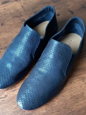 Mörkblå loafers från Alberville i skinn storlek 36 - Snygga mörkblå loafers från Alberville i mjukt perforerat skinn. Skorna har en minimalistisk design utan snörning och en rundad tå. Perfekta för dig som gillar stilrena och bekväma skor med en modern touch.