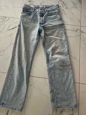 Ljusblå raka jeans - Säljer ett par ljusblå jeans med rak passform och klassisk femficksdesign. Jeansen har hög midja och är tillverkade i denim med en lätt tvättad look. Perfekta för en avslappnad och trendig stil.