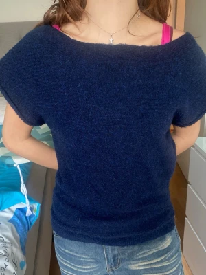 Mörkblå Nelly stickad topp med kort ärm - Mysig mörkblå stickad topp med korta ärmar och bred halsringning. Enkel och stilren design som passar perfekt till jeans eller kjol. Mjuk och skön kvalitet, troligtvis i ull- eller akrylblandning. Knappast använd 