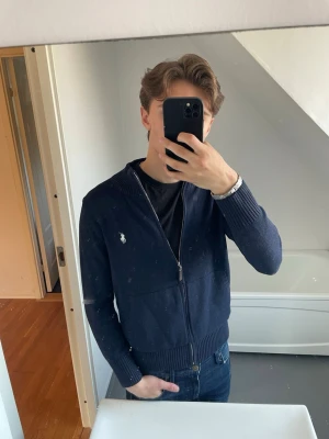 Mörkblå ziptröja från Ralph Lauren - Snygg mörkblå ziptröja från Polo Ralph Lauren med vit broderad logga på bröstet.  Den är i mycket bra skick då den knappt är använd. Den är i storlek S och jag på bilden är 180cm. 