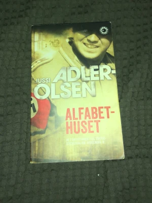 Alfabethuset av Jussi Adler-Olsen - Spännande psykologisk thriller av Jussi Adler-Olsen. Boken utspelar sig under andra världskriget och handlar om två engelska piloter som tvingas gömma sig bland psykiskt sjuka. Pocketbok med gul och röd framsida, tryckt av Bonnier Pocket.