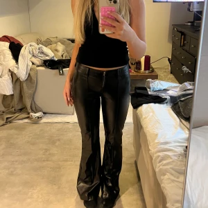Svarta skinnbyxor - Snygga svarta skinnbyxor med hög midja och bootcut-stil. Byxorna har en dragkedja framtill och ger en cool look. Perfekta för att ge en edgy touch till din outfit.