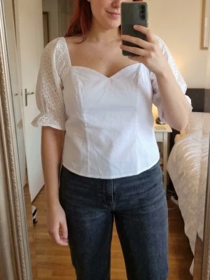 Vit blus med broderade puffärmar - Superfin vit blus från Asos med broderade puffärmar och söt v-ringning. Toppen har en croppad passform och är tillverkad i bomull. Perfekt för dig som gillar romantiska detaljer och vill ha en trendig look. Storlek 42