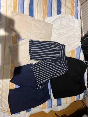 Fem par shorts i olika färger och stilar - Säljer fem par shorts i olika färger: beige, vit, svart, marinblå och ett par blåvitrandiga. Perfekta för sommaren och har bekväm resårmidja. De blåvitrandiga har ett sportigt utseende och de marinblå har snörning i midjan. Passar dig som gillar enkel och avslappnad stil. Storken kan ses på bilderna!