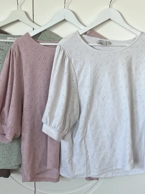 Ett sommar sätt med fyra blusar med blom mönster på - Taupefärgad blus från Indiska med broderat hålmönster och rund halsringning. Blusen har trekvartsärmar med lätt puff och är tillverkad i ett mjukt tyg som känns luftigt och bekvämt. Perfekt för en trendig och romantisk stil.