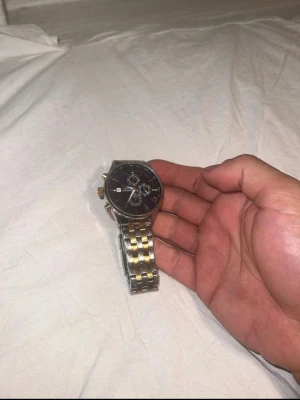 Tvåfärgad kronografklocka från sekonda - Stilren klocka från Curren med blå urtavla, datumvisning och tre subdials. Armbandet är i metall med både silver- och guldfärgade länkar. Klockan har rund boett och detaljer i guld på urtavlan. Perfekt accessoar för dig som gillar klassisk men modern stil.