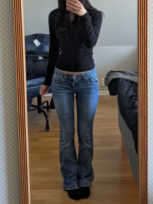 Blå bootcut jeans med låg midja - Säljer ett par klassiska blå bootcut jeans med låg midja och fem fickor. Jeansen har en lätt tvättad look och sitter tajt över låren för att sedan bli vidare nedtill. Perfekta för dig som gillar en retrostil och vill ha ett par snygga jeans till din garderob.