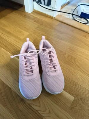 Ljusrosa sneakers med mesh-överdel - Säljer ett par ljusrosa sneakers med klassisk låg profil och vita sulor. Skorna har en ventilerande mesh-överdel och matchande rosa skosnören. Perfekta för dig som gillar en sportig och fräsch stil. Diskreta ränder på sidan ger extra detalj. Andvänts 1 gång inomhus. Storlek 38