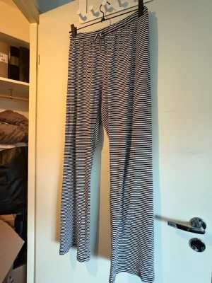 Randiga mjuka loungewear-byxor - Säljer ett par superbekväma loungewear-byxor med svartvita smala ränder och dragsko i midjan. Byxorna har raka ben och är tillverkade i ett mjukt, stretchigt material som passar perfekt för chill dagar hemma.