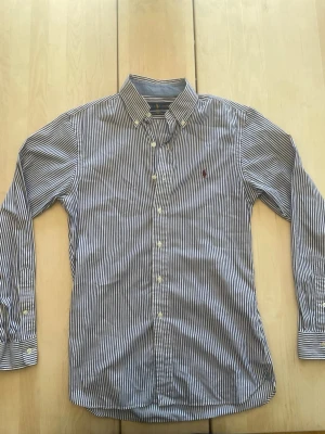Randig Ralph Lauren Skjorta - Tjena! Säljer nu en riktigt snygg blå/vit randig skjorta från Ralph Lauren då den inte används. Den är i mycket fint skick, inga synliga defekter. Skjortan är i en slim passform och är perfekt nu till sommaren! Hör av er vid närmsta fundering🙌