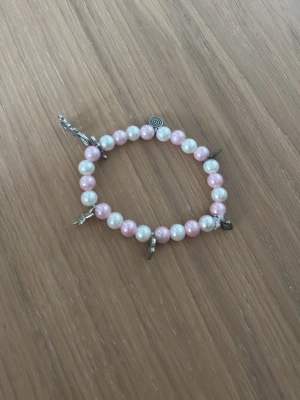 Pärlarmband med berlocker rosa/vit - Sött armband med rosa och vita pärlor, dekorerat med små metallberlocker i olika former. Elastisk tråd gör det enkelt att ta på och av. Perfekt accessoar för att addera lite färg och personlighet till din stil.