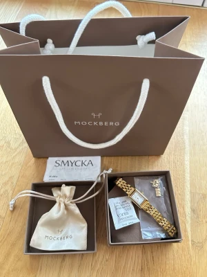Mockberg guldig klocka med länkarmband - Snygg klocka från Mockberg i guld med klassiskt länkarmband och rektangulär urtavla. Klockan levereras i originalask med extra länkar och tygpåse. Perfekt accessoar för att lyfta din stil.