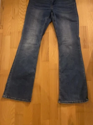 Blå bootcut jeans från Lindex - Snygga blå bootcut jeans från Lindex med klassisk femficksdesign och dragkedjegylf. Jeansen har en lätt tvättad look och utsvängda ben. Perfekta för dig som gillar en retrostil och vill ha ett par bekväma jeans i bomull.