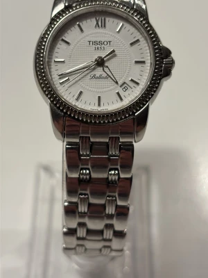Tissot Ballade silverfärgad klocka - Stilren Tissot Ballade klocka i silverfärgat stål med vit urtavla och datumvisning. Klassisk rund form med detaljerad boett och länkarmband i metall. Perfekt accessoar för dig som gillar tidlös design och kvalitet.