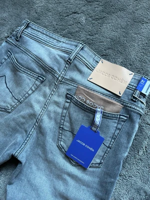 Grå jeans från Jacob Cohën - Snygga grå jeans från Jacob Cohën med klassisk femficksdesign och läderpatch bak. Jeansen har en modern tvätt och diskreta sömmar, perfekt för en stilren look. Materialet är mjukt och stretchigt för extra komfort.