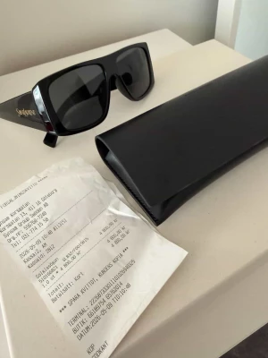 Svarta Saint Laurent solglasögon - Aldrig använda Säljer ett par svarta, rektangulära solglasögon från Saint Laurent med breda skalmar och guldlogga på sidan. 