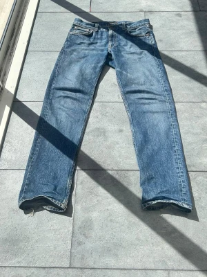 Nudie Jeans - Klassiska blå jeans från Nudie Jeans med rak passform och femficksdesign. Jeansen har en ljus tvätt och är tillverkade i denim. Perfekta för en avslappnad och tidlös stil.