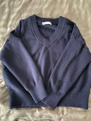 Mörkblå stickad tröja från Bershka - Mysig mörkblå stickad tröja från Bershka med djup V-ringning och breda ribbade muddar vid ärmslut och nederkant. Perfekt för lager-på-lager och enkel att matcha med jeans eller kjol.